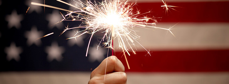 hand holding a lit sparkler in front of American flag