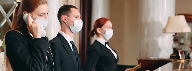 Check in hotel. receptionist at counter in hotel wearing medical masks as precaution against virus.