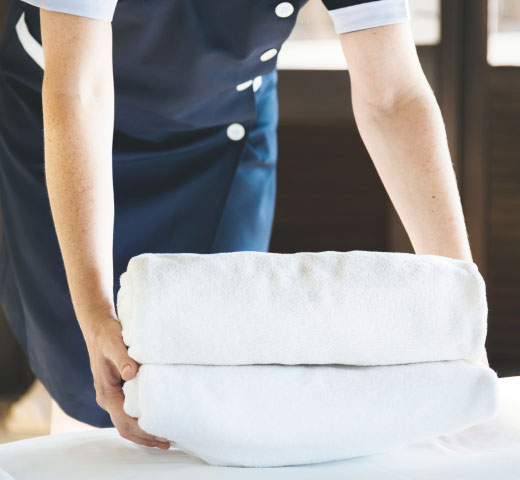 Maid putting towels on bed in hotel room