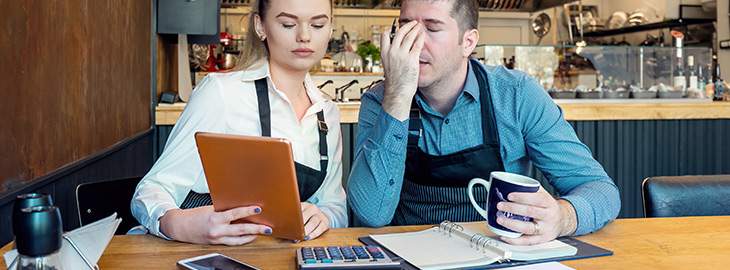 Worried owners in empty restaurant calculating finances