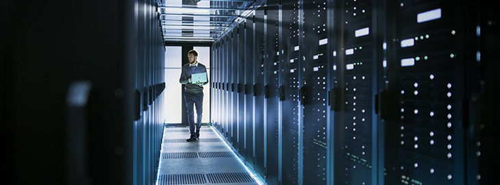 IT Technician Works on Laptop in Big Data Center full of Rack Servers