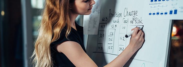 Businesswoman evaluating risks of a business strategy drawing a chart on whiteboard standing in a conference room